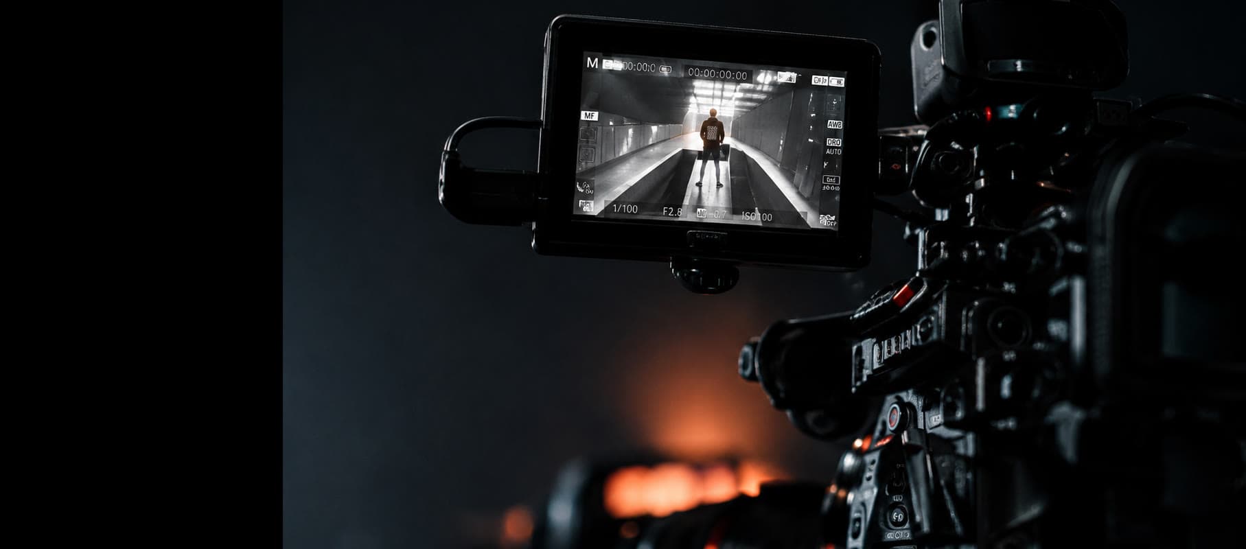 Cinema camera and its monitor on set, warm practicals burning out of focus behind